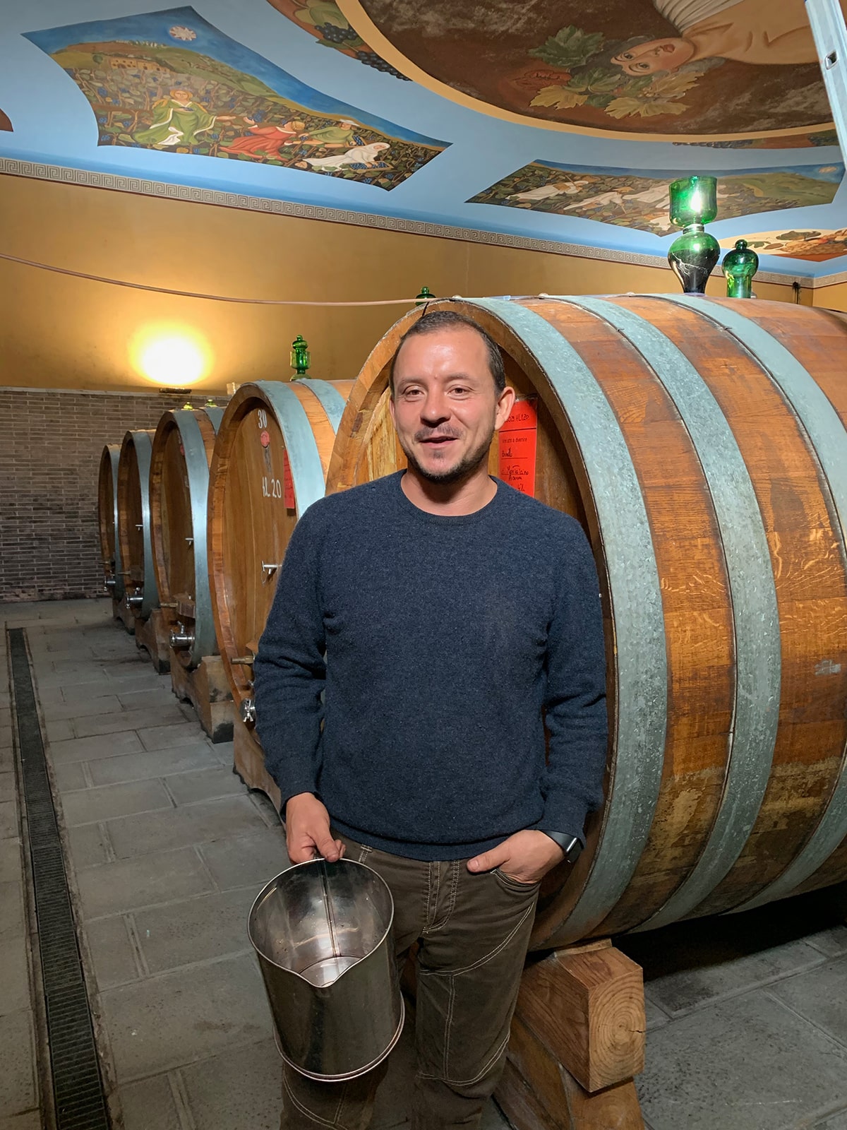 Man inside of a wine cellar standing next to 5 foot tall wine barrels